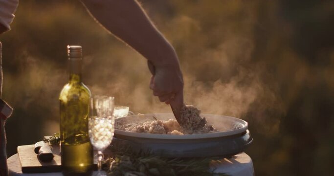 Female cooking hand spatula stirs risotto steam golden light close up