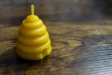 A beehive votive shaped beeswax candle is sitting on a wood table.