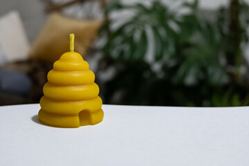 A beehive votive shaped beeswax candle is sitting on white paper with plants in the background.