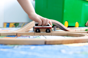A hand holds a children's car on a wooden road constructor, soft selective focus.