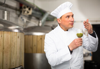 Skilled man brewmaster smelling hops pellets to evaluate quality in workshop of beer factory.