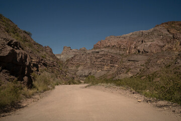 Travel. View of the dirt road across the arid desert and colorful rock formations.