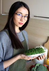 Young Asian woman holding microgreens in her hands. Vegetarian woman. Reusable package.