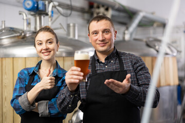 Happy woman and man craft brewery owners inviting to tasting fresh amber beer of own production....