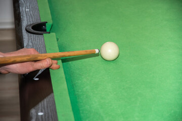 Hand with cue aiming on billiard ball at table

