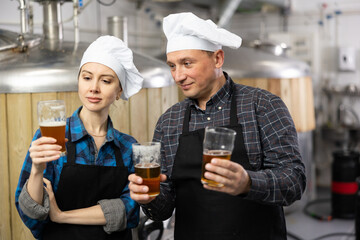 Brewers man and woman is standing with glasses for beer on his workplace indoor