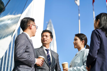 group of asian business people standing chatting on street in downtown