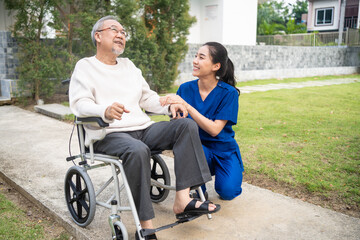 Asian caregiver nurse take care senior male sit on wheelchair outdoor. 