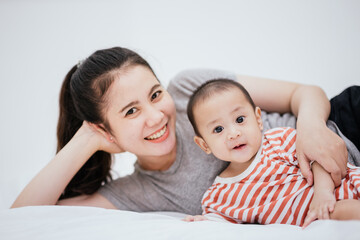 Asian mom enjoy with baby adorable on the bed is smiling and happy. Happy family. Unconditional love infant baby.