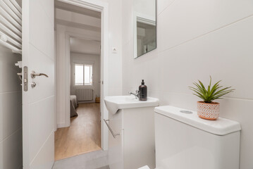 Bathroom with frameless square mirror, white porcelain sink on gloss white wooden cabinet, white heated towel rail behind the wall and decorative plant
