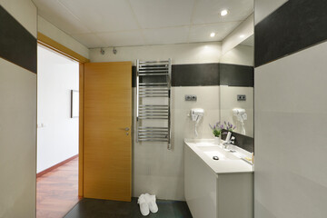 Bathroom with chrome heated towel rail, frameless mirror and white bath slippers