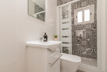 Bathroom with frameless square mirror, white porcelain sink on glossy white wooden cabinet, shower tray with screen and wall covered with hydraulic tiles