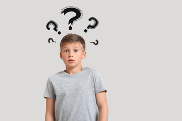 Portrait of shocked little boy and question marks on light background