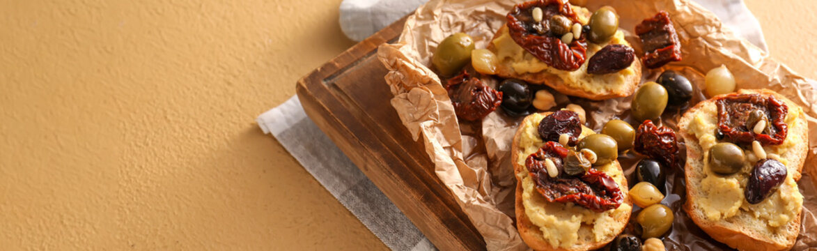 Tasty bruschettas with sun-dried tomatoes, olives and hummus on color background with space for text