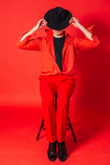 Tall handsome man dressed in red shirt, trousers and black hat posing on the red background