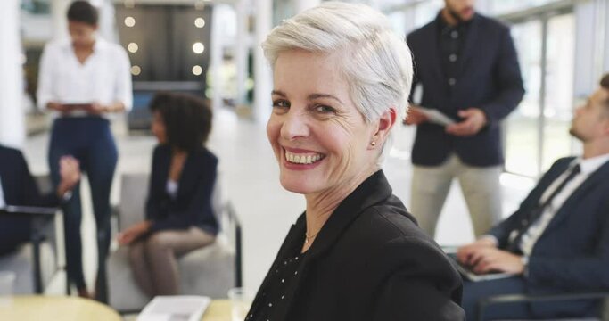 Dedicated leaders make all the difference to the team. 4k video footage of a mature businesswoman smiling in an office with her colleagues in the background.