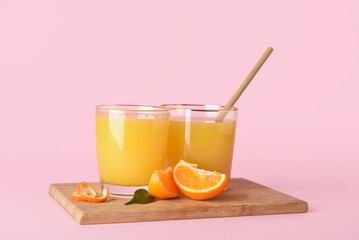 Glasses of fresh tangerine juice on pink background
