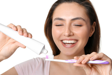 Young woman applying tooth paste onto brush on white background, closeup