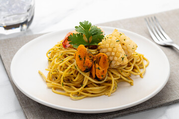 Seafood spaghetti with blue mussels, squids and shrimps served on a white plate placed on a gray place mat.