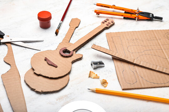 Cardboard guitar toy with stationery supplies on light background