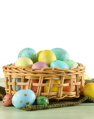 Wicker basket of painted Easter eggs on table against white background