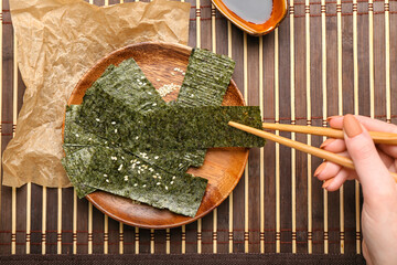 Woman eating tasty seaweed sheets at table © Pixel-Shot