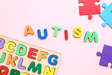 Word AUTISM with puzzle pieces and letters on pink background