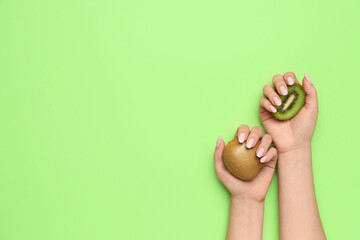 Woman with beautiful manicure holding kiwi on green background, closeup