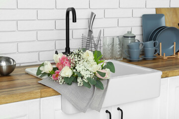 Sink with beautiful flowers and kitchenware on counters near white brick wall