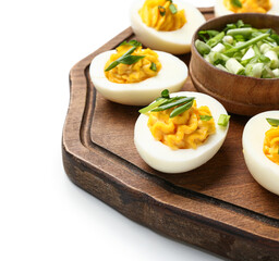 Board with tasty stuffed eggs and green onion on white background, closeup. Easter celebration