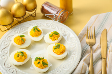 Plate with stuffed eggs, cutlery, napkin and spices on yellow background, closeup. Easter celebration