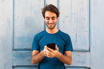 Happy young caucasian man holding mobile phone reading text message outdoors. Copy space.