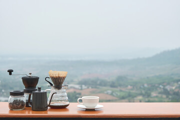 dripping coffee set with grinder jar coffee beans on the table at countryside mountain view in the morning with blurred faded mist background