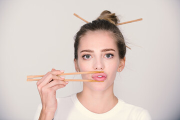 Sexy young woman at a sushi bar touch sensual lips with chopsticks. Sushi advertising. Studio isolated portrait.