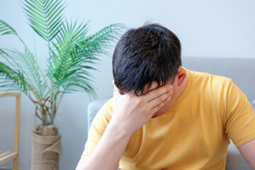 Man in yellow t-shirt covers his face with his hand, the concept of depression and stress.