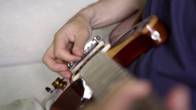 the hand of a white guitarist plays with a plastic plectrum arpeggio on the metal strings of a beautiful lacquered brown electric guitar with two humbucker pickups. neck side view