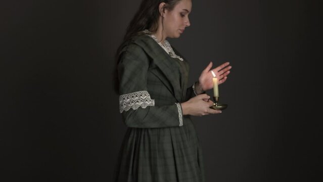 A Victorian woman with long, dark hair walking alone carrying a candle