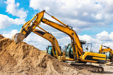 Two powerful excavators work at the same time on a construction site, sunny blue sky in the...