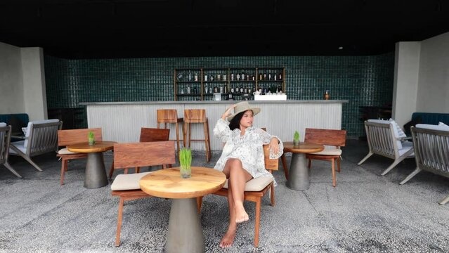 young asian female model with a hat sitting in a chair at an open bar resort on a sunny summer day