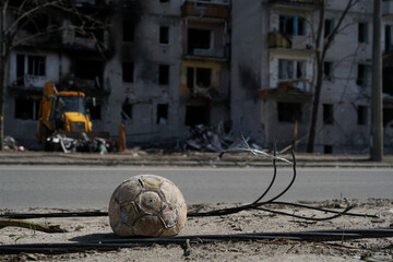 A children's soccer ball lies near the road against a building destroyed by an explosion in the war...