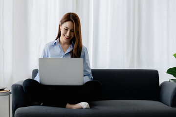 Woman plays on laptop on the sofa in her living room at home, she is resting on weekends after a hard day's work, she relaxes by watching movies and listening to music on her tablet. Holiday concept.