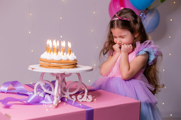 cute little girl in a beautiful dress makes a wish and blows out the candles on the birthday cake....