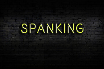 Neon sign. Word spanking against brick wall. Night view