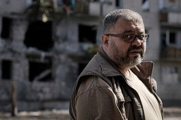 Portrait of a man who looks at his destroyed house, which was hit by a shell from military...