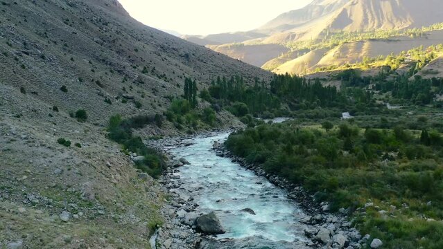 Aerial drone of a glacier river flowing through the mountains of Astore Valley in Pakistan during a sunset afternoon in the summer