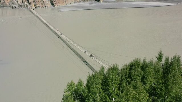 Aerial top down view of tourists crossing the famous Hussaini bridge in Hunza Pakistan with a fast river flowing below and a green forest