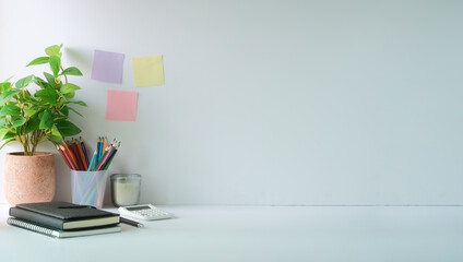 Creative workplace with potted plant, stationery, calculator and colourful sticky notes on light wall.