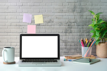 Creative workplace, empty picture frame, coffee cup and supplies on white table with colourful sticky notes on brick
