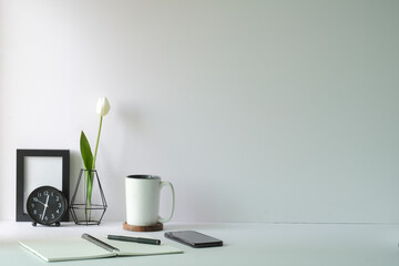 Minimal workplace with picture frame, coffee cup, mobile phone and notebook on white table. Copy space for advertise text or information content.