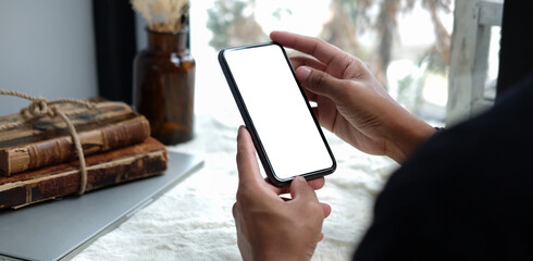 Close up view young man sitting at home office desk and using smart phone. Blank screen for your text message or information content.
